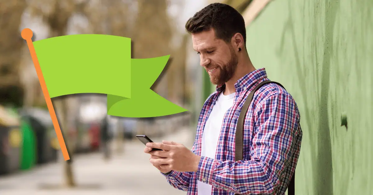 man smiling at phone with green flag icon next to him